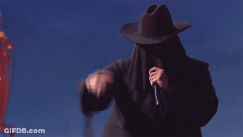 A Man Wearing A Cowboy Hat Covering His Face Holds A Microphone GIF