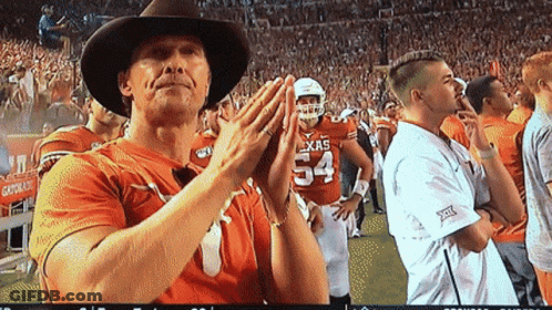 A Man Wearing A Cowboy Hat Is Clapping In Front Of A Player Wearing A Texas Jersey GIF