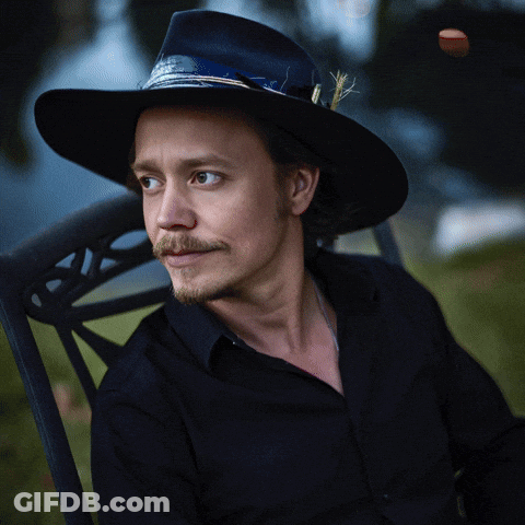 A Man Wearing A Cowboy Hat Is Sitting In A Chair With The Letter B Visible GIF