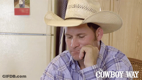 A Man Wearing A Cowboy Hat Is Sitting In Front Of A Cowboy Way Sign GIF