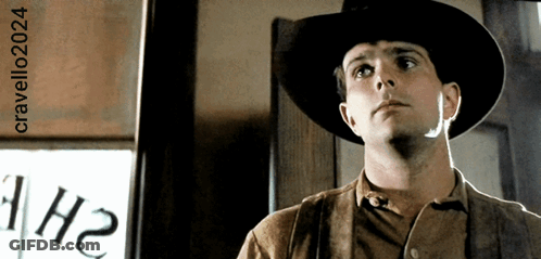 A Man Wearing A Cowboy Hat Is Standing In Front Of A Sign That Says 1H2 GIF