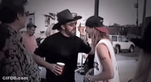 A Man Wearing A Cowboy Hat Is Talking To Another Man While Holding A Cup . GIF