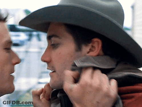 A Man Wearing A Cowboy Hat Is Touching The Face Of Another Man GIF