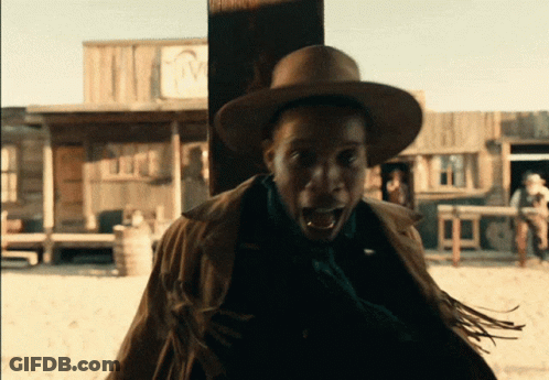 A Man Wearing A Cowboy Hat Stands In Front Of A Building With The Letter M On The Front GIF