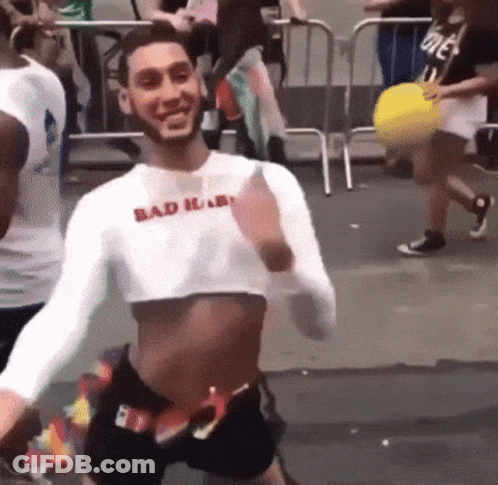 A Man Wearing A Crop Top And Shorts Is Dancing In A Crowd . GIF