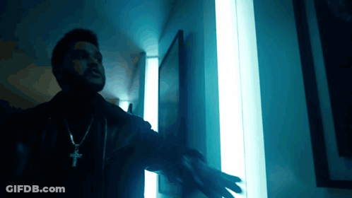A Man Wearing A Cross Necklace Is Standing In Front Of A Blue Light GIF