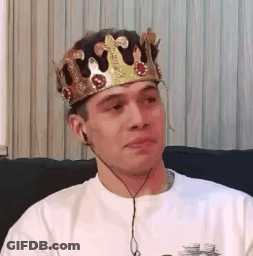 A Man Wearing A Crown Is Sitting On A Couch With Headphones . GIF
