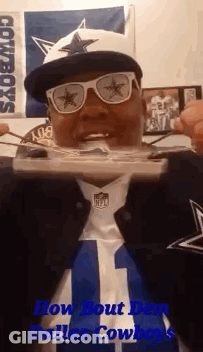 A Man Wearing A Dallas Cowboys Hat , Sunglasses , And A Cowboys Jersey Is Eating Food . GIF