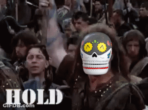 A Man Wearing A Day Of The Dead Mask Stands In Front Of A Crowd Of People With The Word Hold Below Him GIF