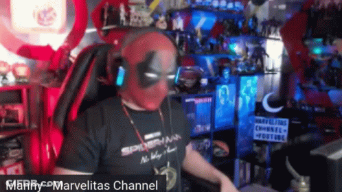 A Man Wearing A Deadpool Mask And Headphones Is Sitting In A Chair . GIF