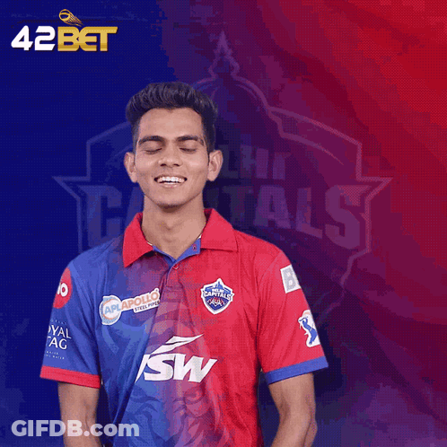 A Man Wearing A Delhi Capitals Shirt Stands In Front Of A Blue And Red Background GIF