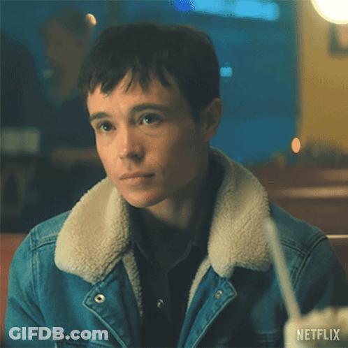 A Man Wearing A Denim Jacket And A Sherpa Collar Is Sitting At A Table With A Drink In His Hand . GIF