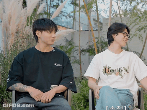 A Man Wearing A Dior Tear T-Shirt Sits Next To A Man Wearing A Black Shirt GIF