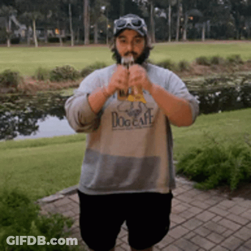A Man Wearing A Dog Cafe Shirt Is Standing In Front Of A Golf Course GIF