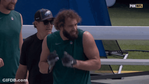 A Man Wearing A Eagles Hat Stands Next To A Man Wearing A Black Shirt GIF