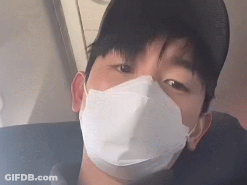 A Man Wearing A Face Mask And A Baseball Cap Is Sitting On A Plane . GIF