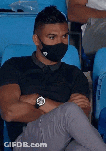 A Man Wearing A Face Mask And A Watch Is Sitting In A Stadium . GIF