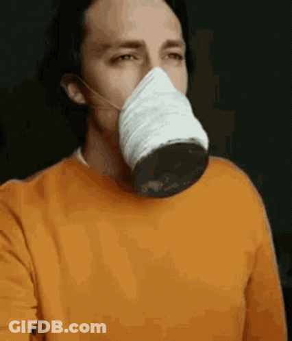 A Man Wearing A Face Mask And An Orange Sweater Is Taking A Selfie . GIF