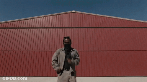A Man Wearing A Face Mask Is Dancing In Front Of A Red Building GIF