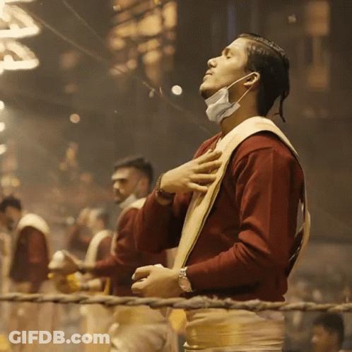 A Man Wearing A Face Mask Stands With His Eyes Closed And His Hands On His Chest GIF
