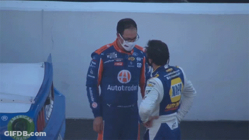 A Man Wearing A Face Mask Talks To Another Man Wearing A Nascar Uniform GIF