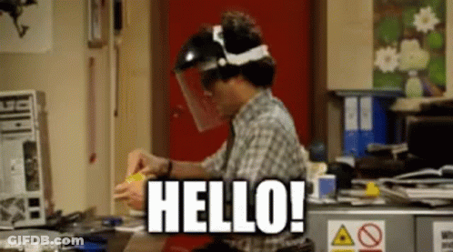 A Man Wearing A Face Shield Is Sitting At A Desk And Says Hello . GIF