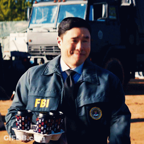 A Man Wearing A Fbi Jacket Carrying A Tray Of Coffee Cups GIF