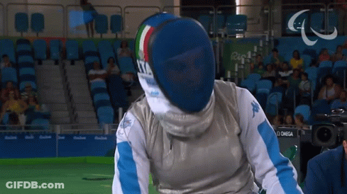 A Man Wearing A Fencing Mask Is Standing In Front Of A Camera That Says Omega GIF