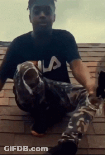 A Man Wearing A Fila Shirt Sits On A Rooftop GIF