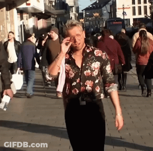 A Man Wearing A Floral Shirt Is Walking Down A Street GIF
