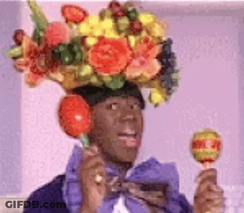A Man Wearing A Flowered Hat Is Holding A Lollipop In His Hand . GIF