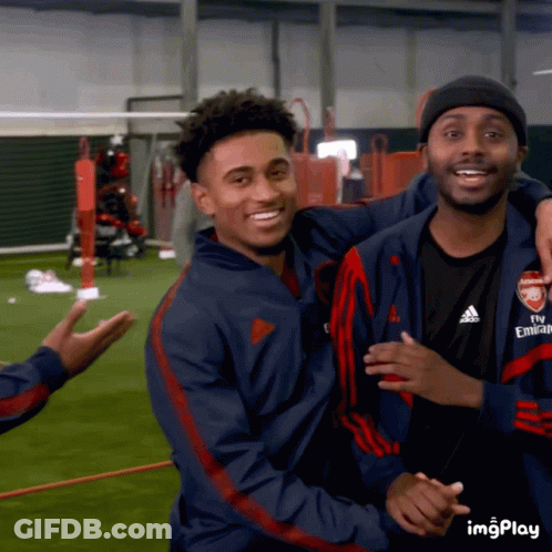 A Man Wearing A Fly Emirates Jacket Hugs Another Man On A Field GIF