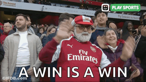 A Man Wearing A Fly Emirates Jersey Stands In A Crowd Of People GIF