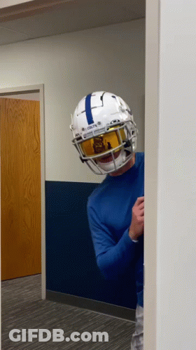 A Man Wearing A Football Helmet And Goggles Is Standing In A Hallway . GIF