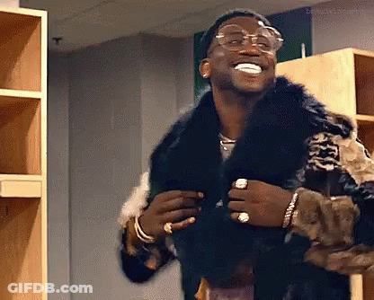A Man Wearing A Fur Coat And Glasses Is Standing In A Locker Room . GIF