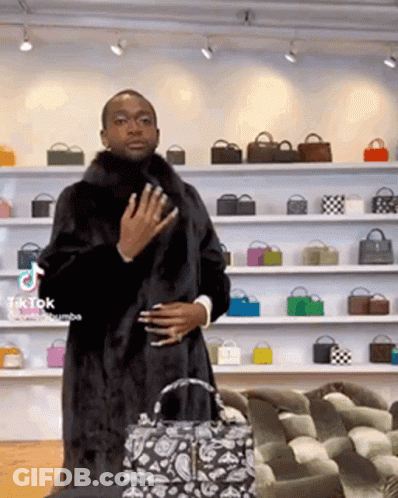 A Man Wearing A Fur Coat Is Standing In Front Of A Wall Of Bags . GIF