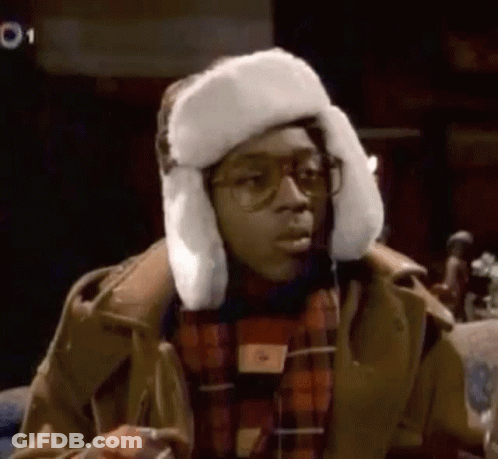 A Man Wearing A Fur Hat And Glasses Is Sitting Down . GIF