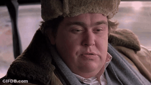 A Man Wearing A Fur Hat And Scarf Is Sitting In A Car And Looking At The Camera . GIF