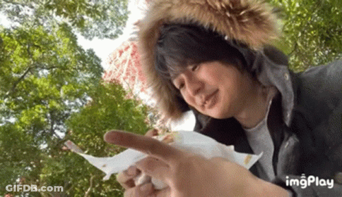 A Man Wearing A Fur Hood Is Holding A Piece Of Paper In His Hand . GIF