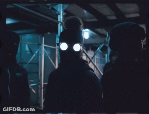 A Man Wearing A Gas Mask And Glasses Stands In The Dark GIF