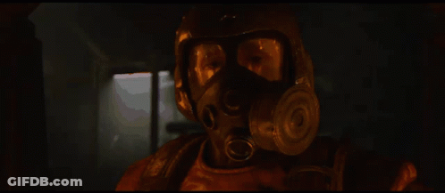 A Man Wearing A Gas Mask And Goggles Looks At The Camera With A Window In The Background GIF