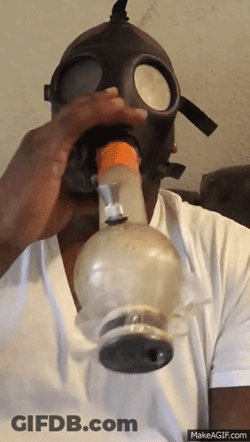 A Man Wearing A Gas Mask Is Blowing Smoke Out Of A Bong GIF