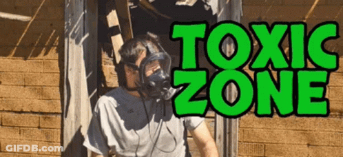 A Man Wearing A Gas Mask Stands In Front Of A Sign That Reads Toxic Zone GIF