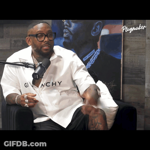 A Man Wearing A Givenchy Shirt Sits In Front Of A Playmaker Poster GIF