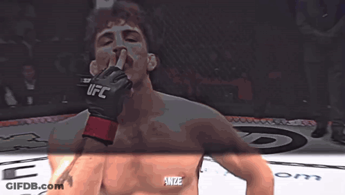 A Man Wearing A Glove That Says UFC Holds His Finger To His Mouth GIF