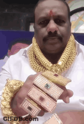 A Man Wearing A Gold Necklace And Bracelets Is Holding A Bracelet That Says ' A ' GIF