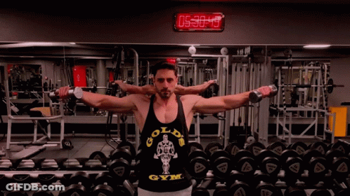 A Man Wearing A Gold 'S Gym Tank Top Is Lifting Dumbbells In A Gym GIF