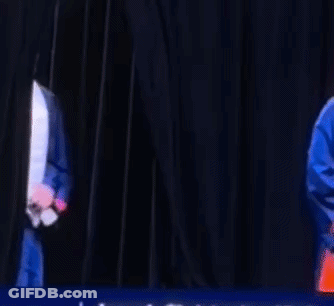 A Man Wearing A Graduation Cap And Gown Is Dancing On A Stage . GIF