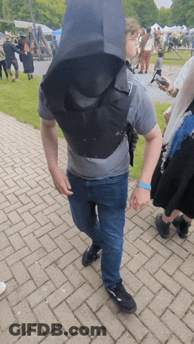 A Man Wearing A Gray Shirt And Blue Wristband Walking On A Brick Sidewalk GIF