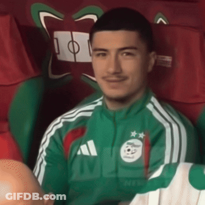 A Man Wearing A Green Adidas Jacket Is Sitting In A Chair GIF